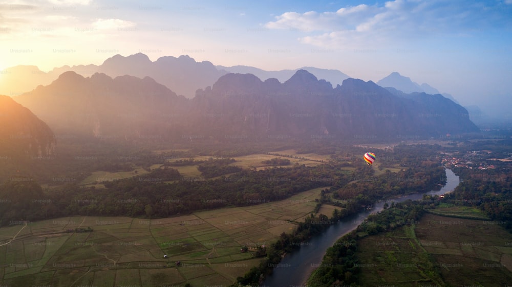 Luftaufnahme von Vang Vieng mit Bergen und Ballon bei Sonnenuntergang.