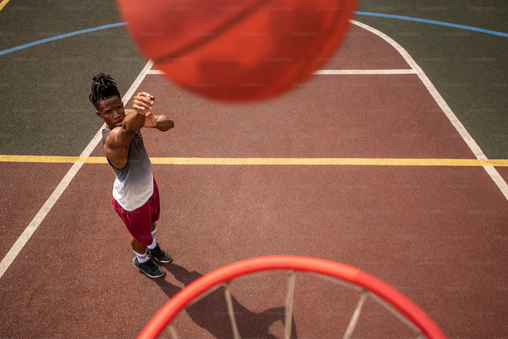 African young sportsman throwing ball in basket while standing on the court during training