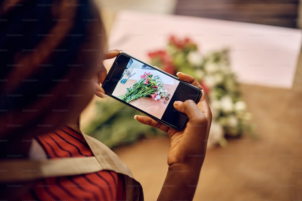 Primer plano de una florista femenina usando un teléfono inteligente y tomando una foto del ramo de flores en la floristería.