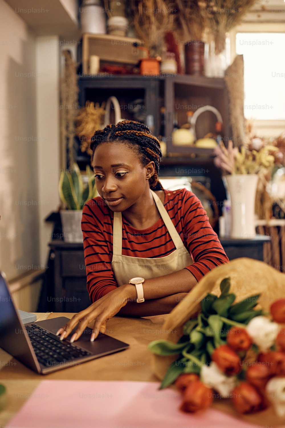 Young African American florist using laptop while working at her flower shop.