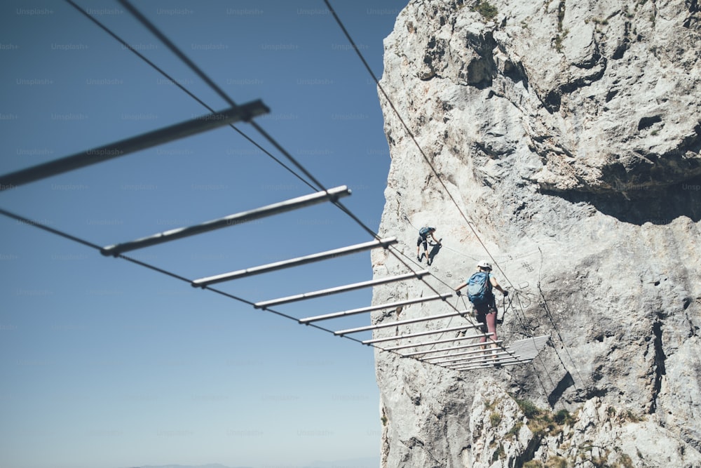 Two women climbers moving up and crossing wire bridge on via ferrata route.
