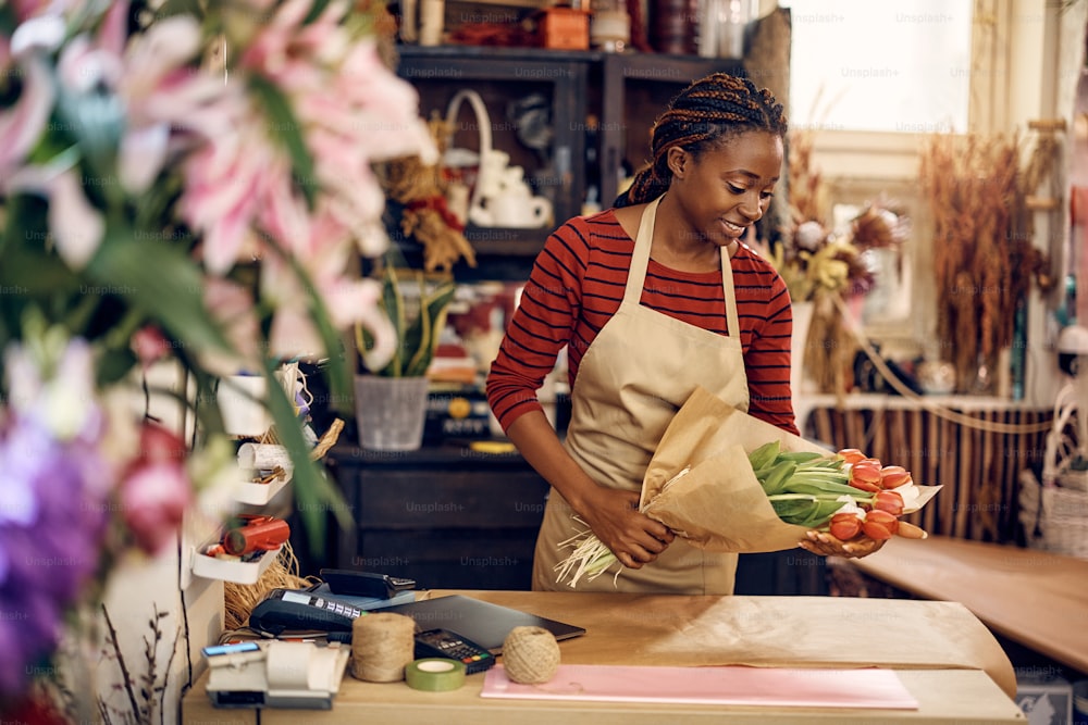 Happy African American woman making bouquet of tulips while working at flower shop.