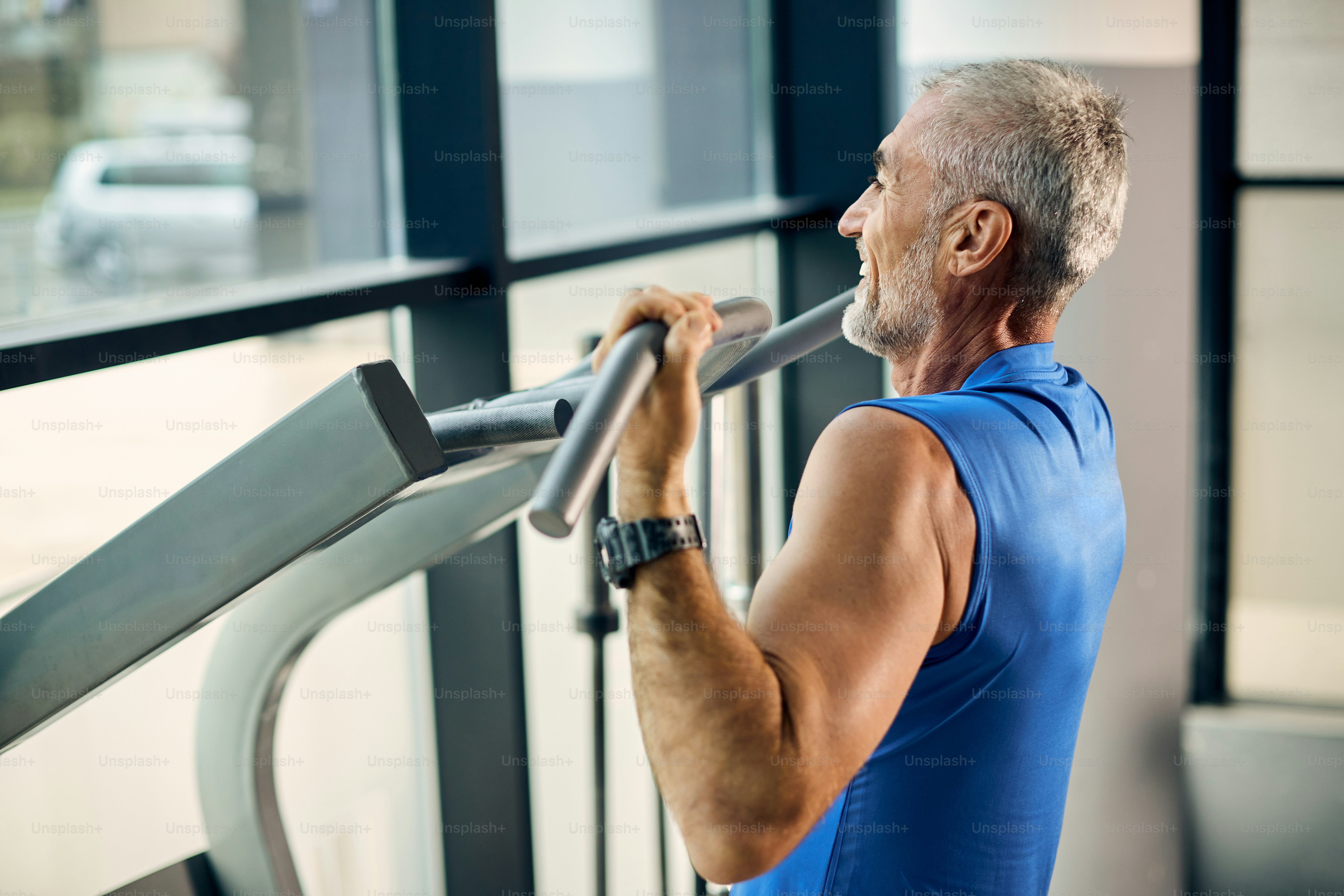 Happy mature athlete practicing pull-ups while working out at health club.