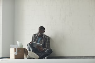 African man sitting on the floor in empty room and using digital tablet he working online