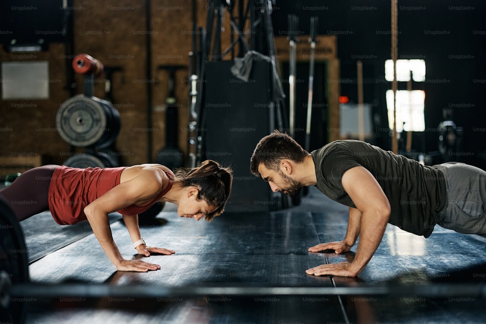 Couple d’athlètes exerçant des pompes pendant un entraînement croisé dans une salle de sport. Espace de copie.