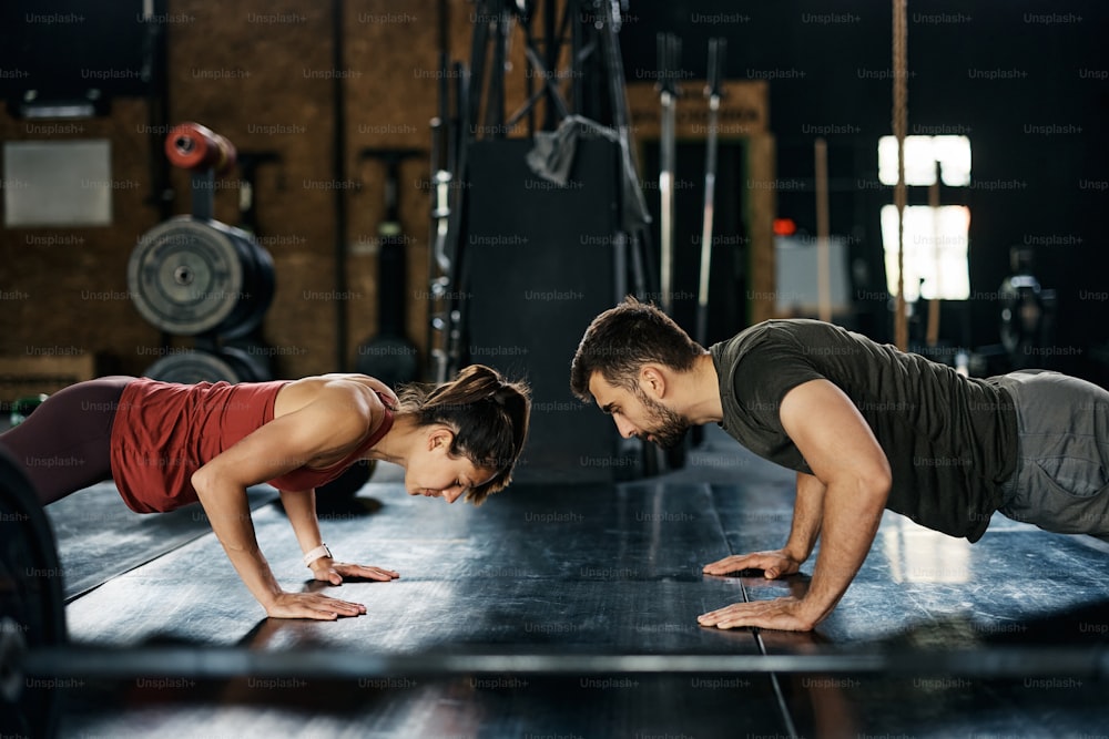 Athletic couple exercising push-ups during cross training in a gym. Copy space.