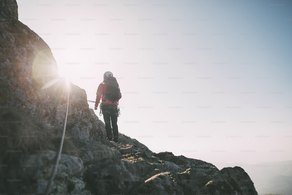 Vista trasera de un hombre completamente equipado escalando una montaña a lo largo de una vía ferrata.