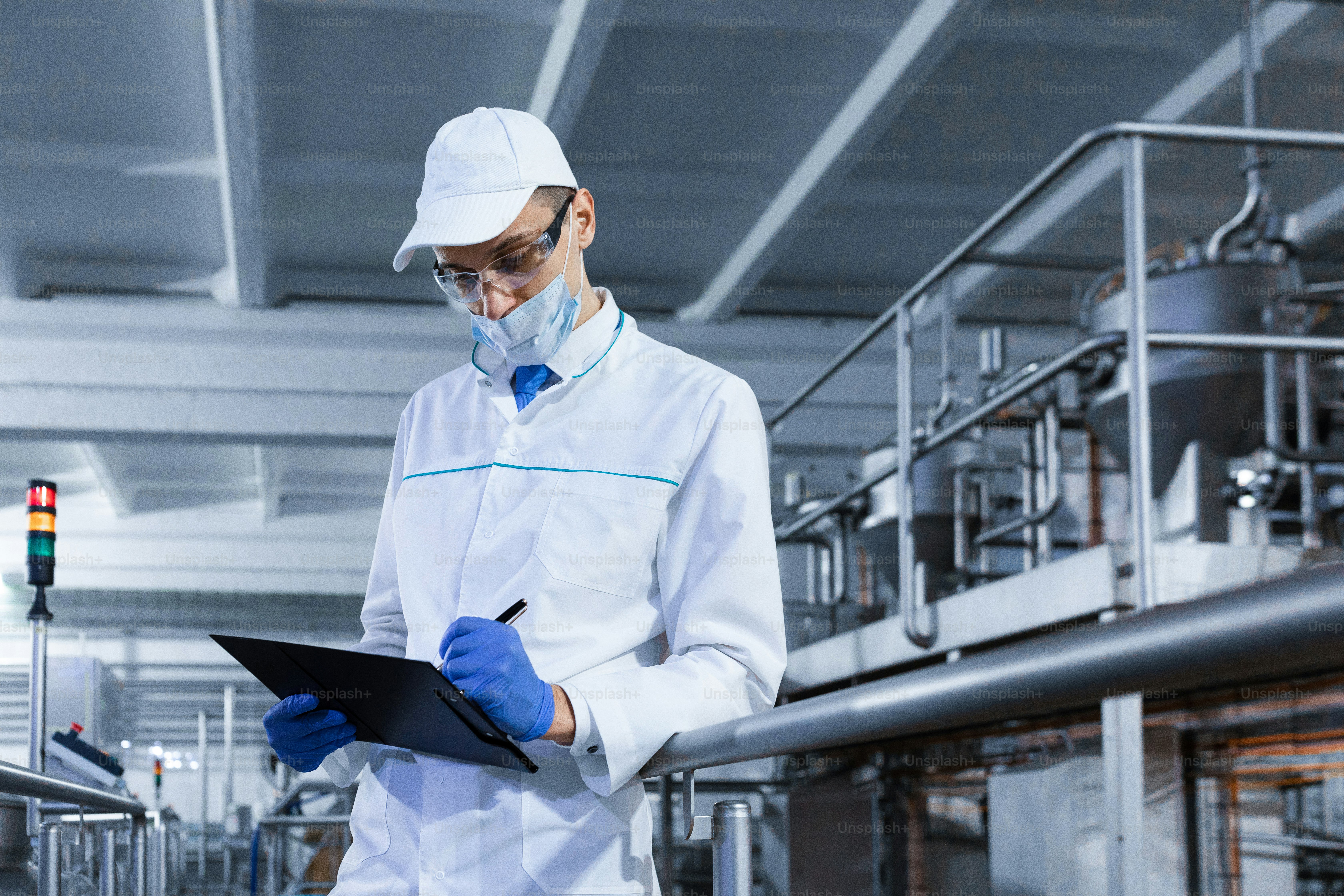 Technologe in der Mütze, Maske und weißem Kittel steht in der Produktionshalle und macht Notizen mit einem Stift im Blatt. Der Inspektor entfernt die Indikatoren in der Molkerei. Ingenieur führt Statistiken über die Produktion