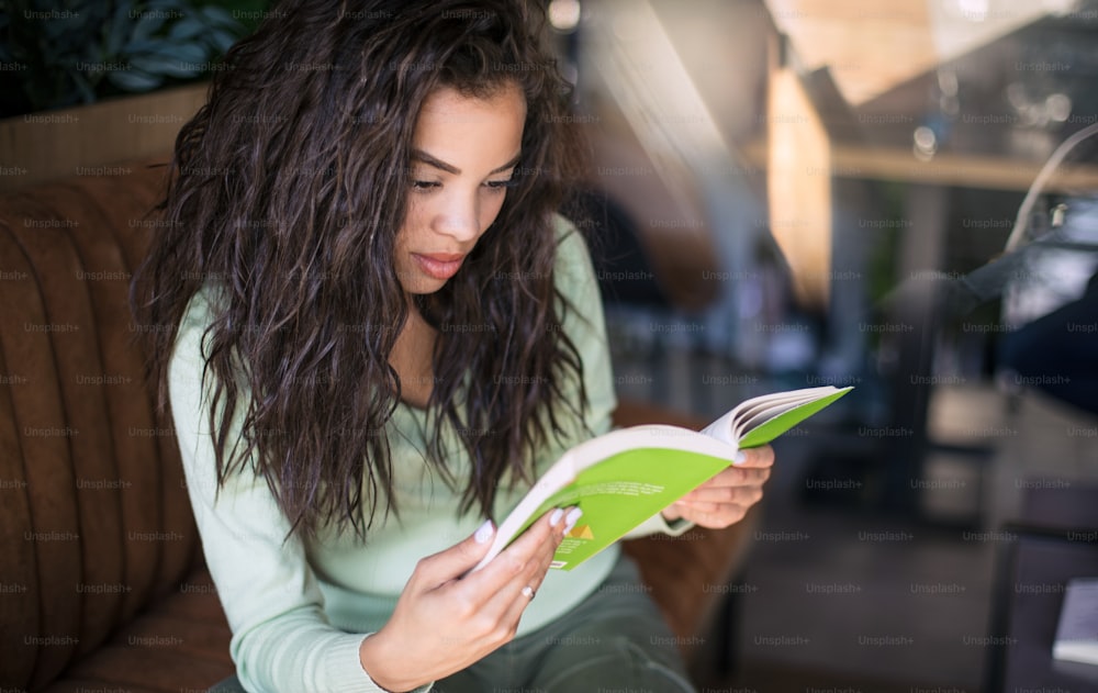 Through reading we learn new things. Young student girl at cafe reading book.