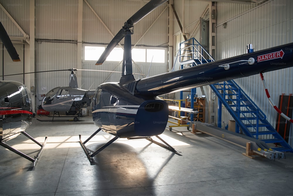 Dois helicópteros civis modernos de pé ao lado de aeronaves com fuselagem de cauda desmontada