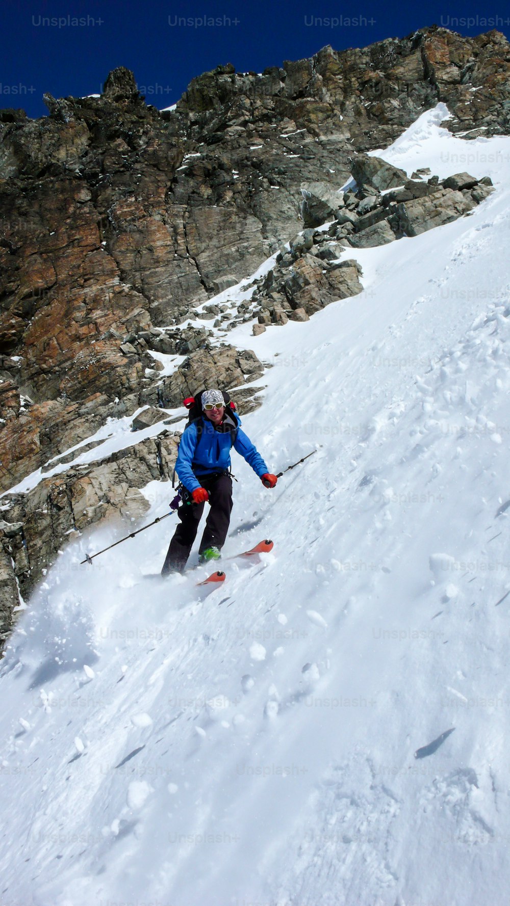 männlicher Extremskifahrer, der im tiefen Winter in den Schweizer Alpen bei Klosters an einem schönen Wintertag ein sehr steiles Couloir hinunterfährt