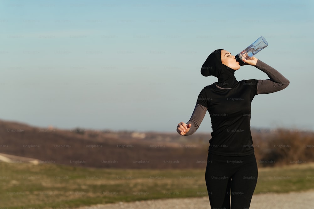 Young athletic woman refreshing herself with water while running in nature. Copy space.