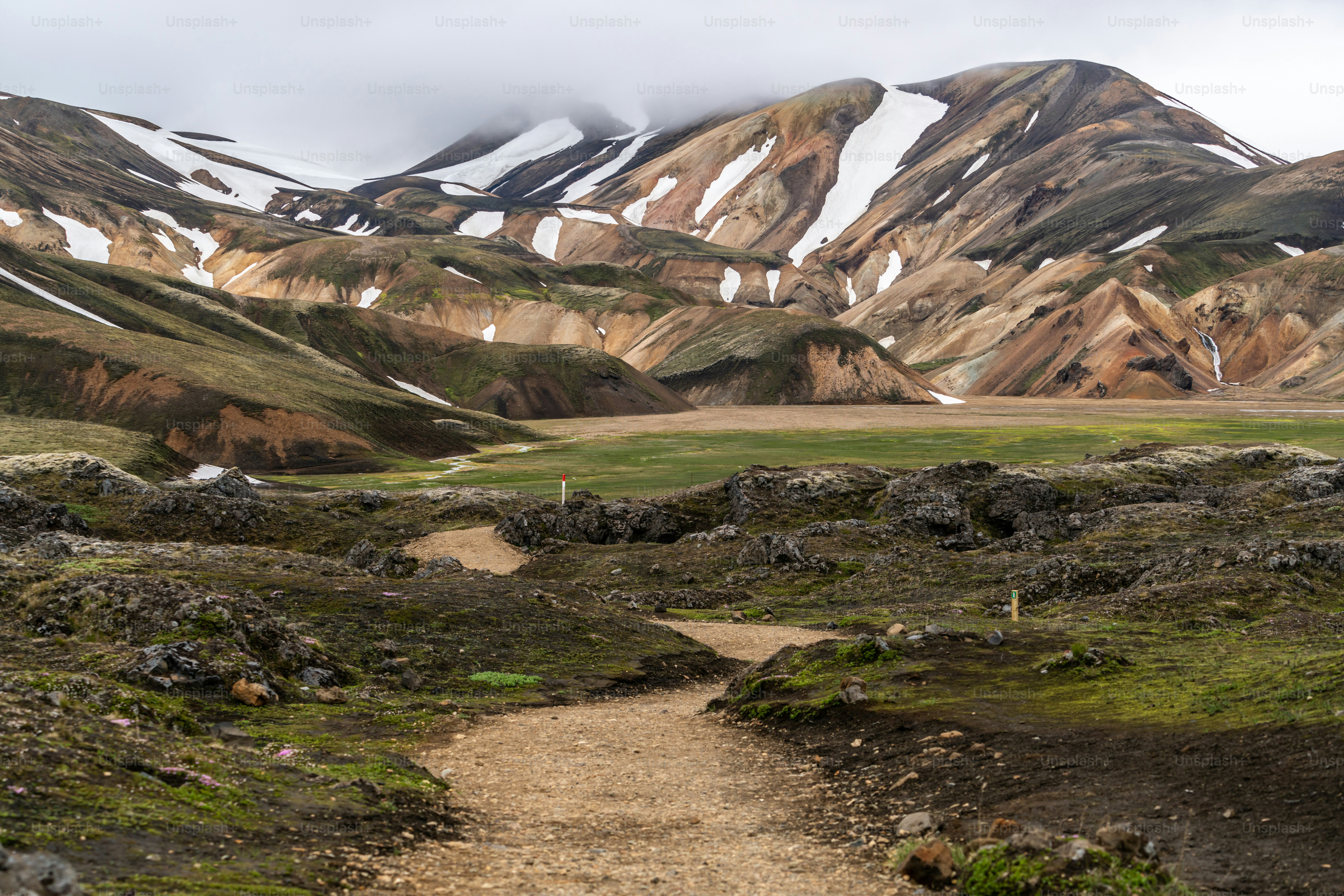 Ein unbefestigter Wanderweg durch eine felsige Landschaft zu schneebedeckten Bergen in Island