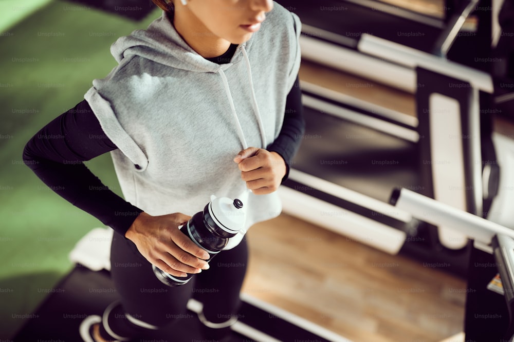 Close-up of female athlete holding water bottle while jogging on running track in a gym.