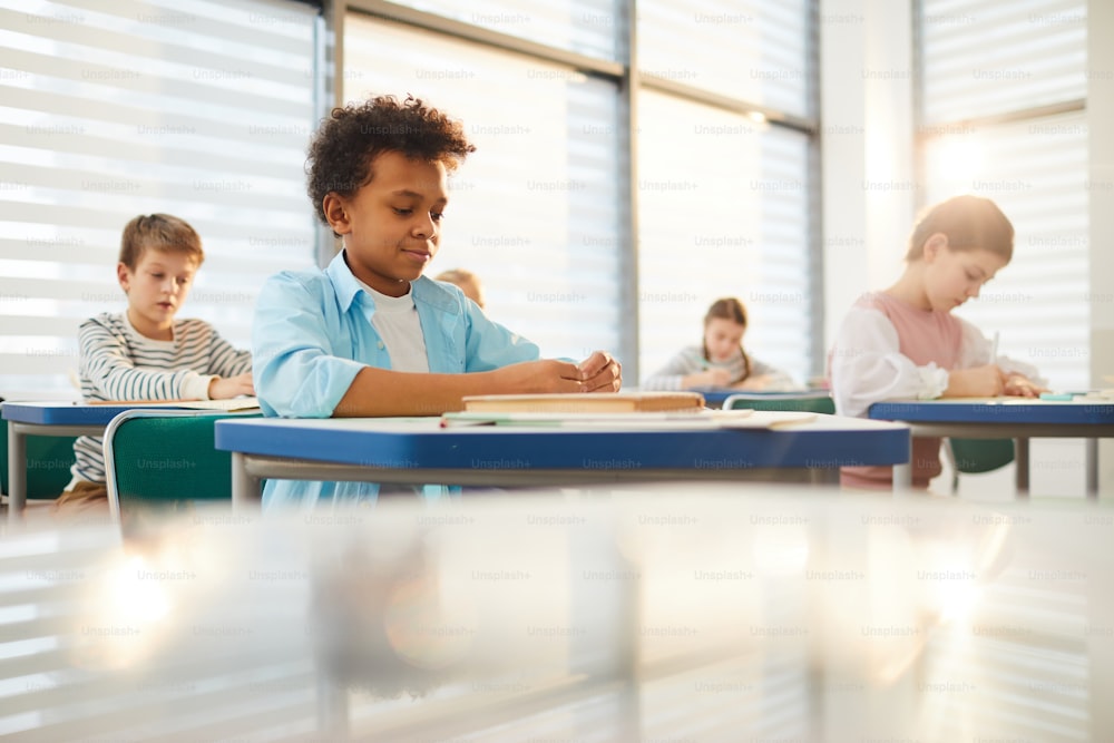 Foto horizontal de jovens do ensino médio vestindo roupas casuais sentados em carteiras na sala de aula moderna fazendo exercícios de aula, espaço de cópia