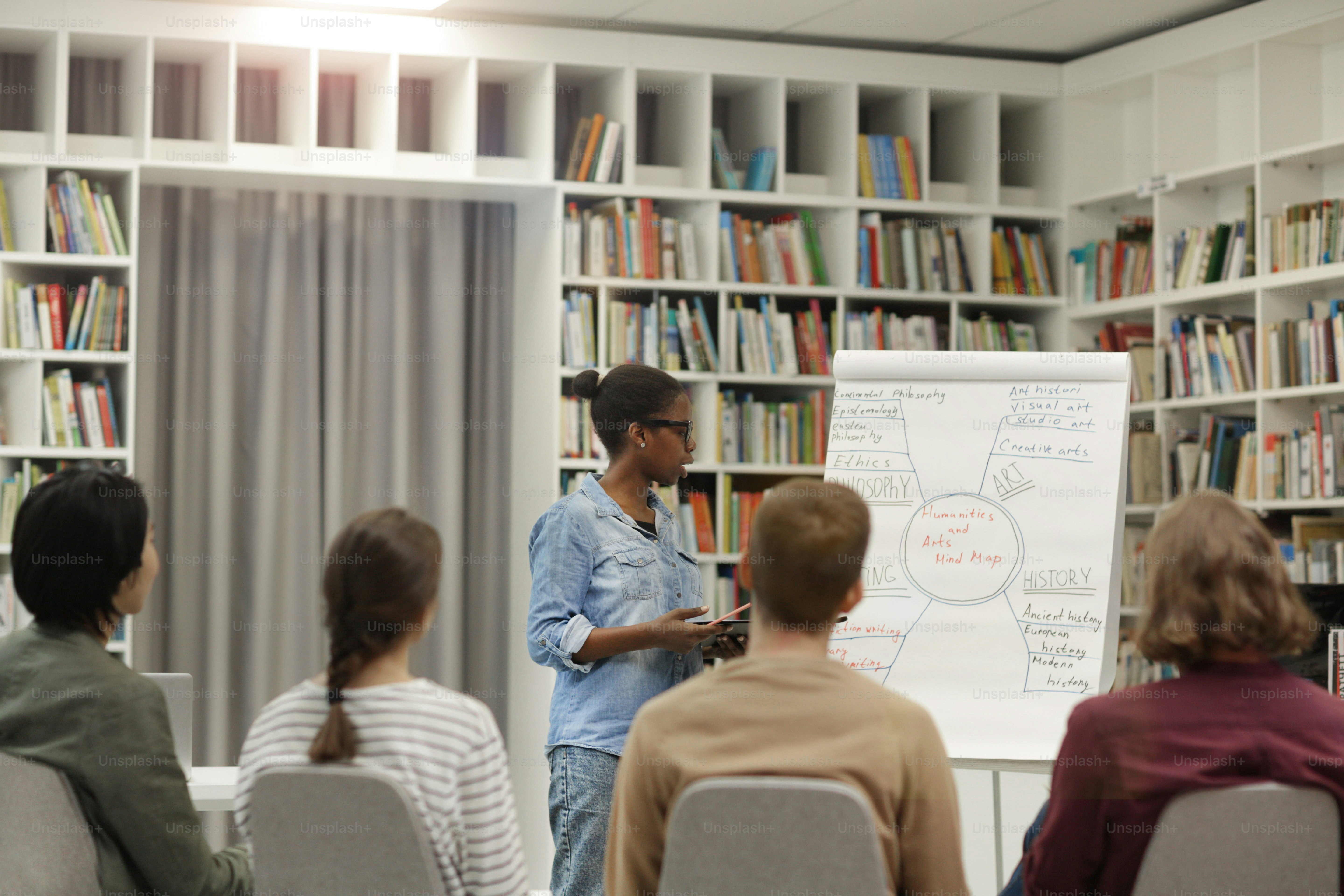 Jeune femme africaine pointant du doigt le tableau blanc et tenant la présentation pour les jeunes dans la bibliothèque