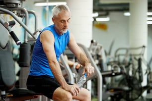 Mature male athlete drinking water while taking a break from exercising in a gym.