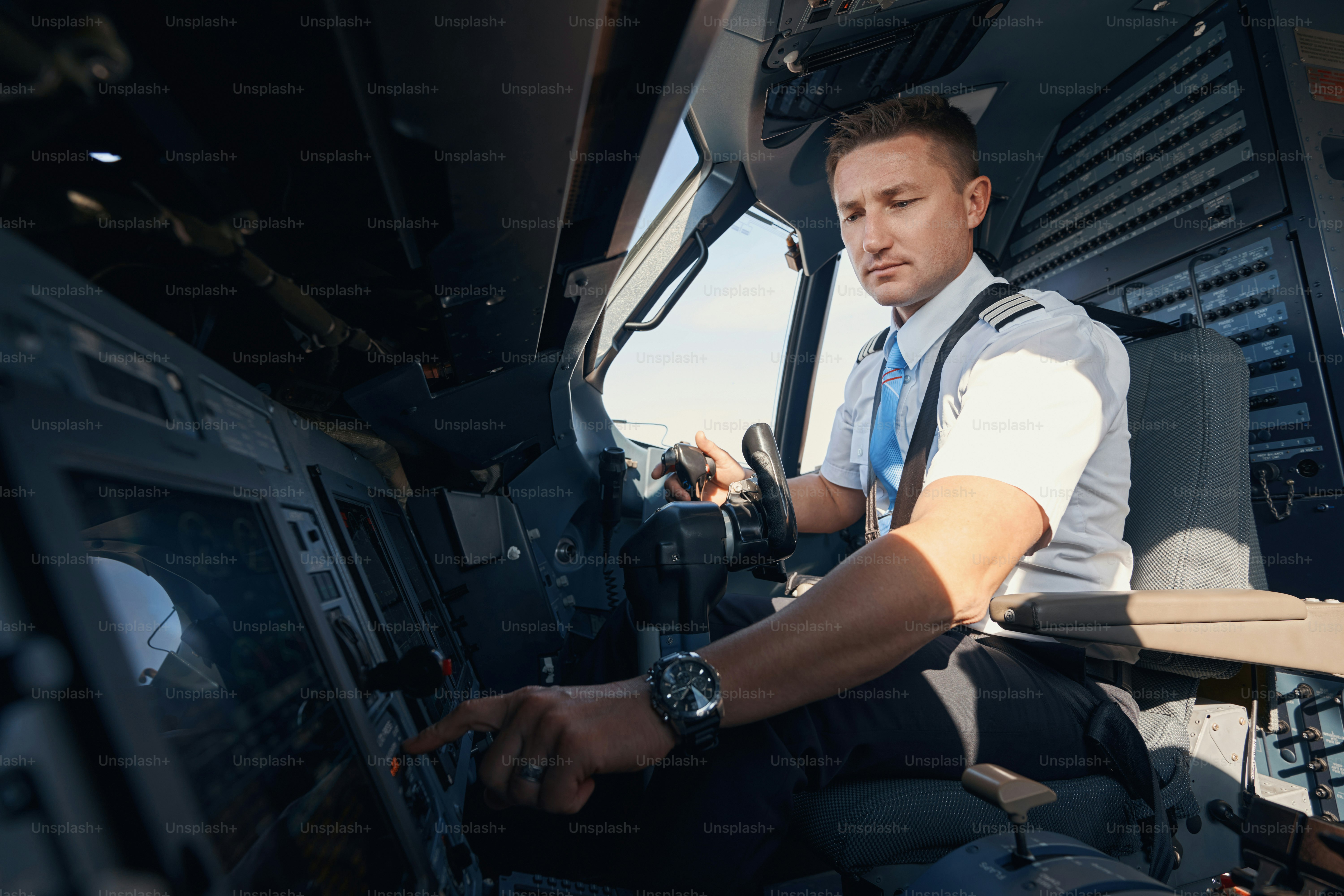 Sideway photo of Caucasian second pilot in uniform pushing control panel button on dashboard