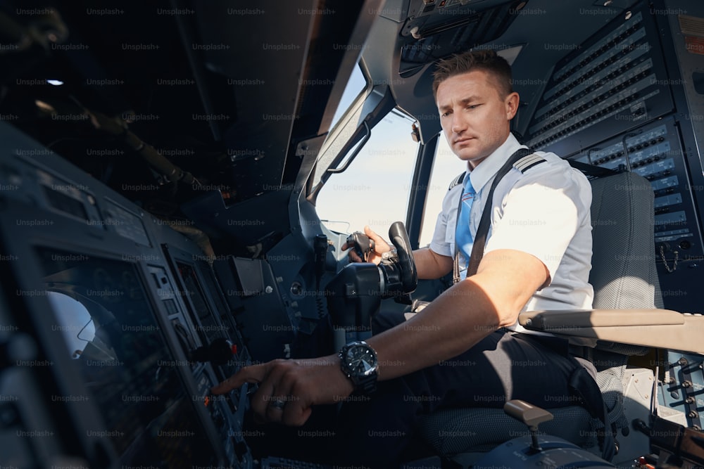 Sideway photo of Caucasian second pilot in uniform pushing control panel button on dashboard