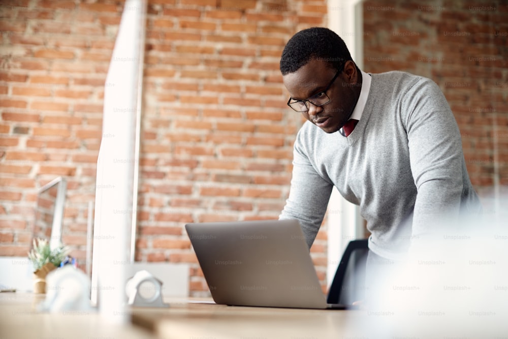 Empreendedor afro-americano usando laptop enquanto trabalha em escritório corporativo. Espaço de cópia.