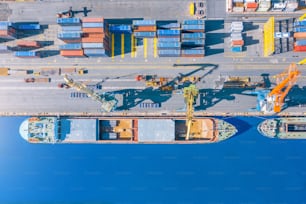 Vue aérienne de dessus d’un énorme cargo amarré à l’embarcadère du port, chargeant des marchandises, du métal, du béton et d’autres matières premières solides