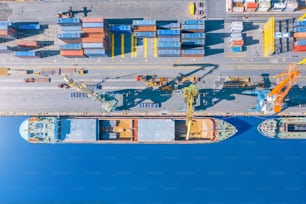 Aerial top view huge cargo ship moored at the pier at the port, loading goods, metal, concrete and other solid raw materials