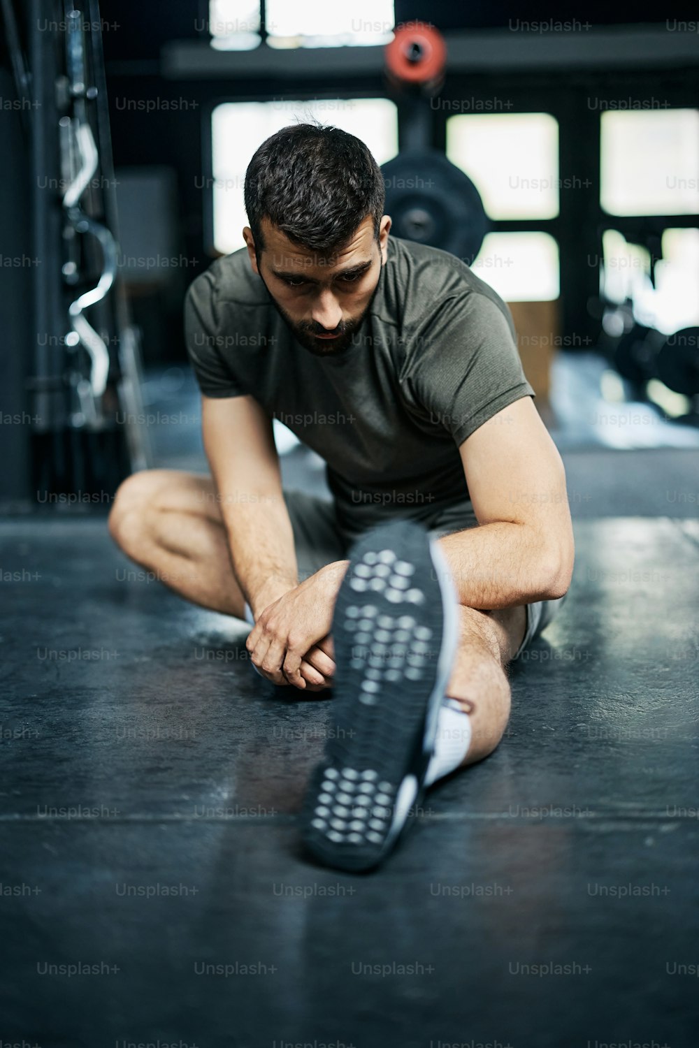 Männlicher Athlet, der seine Beine beim Aufwärmen für das Sporttraining in einem Fitnessstudio streckt.