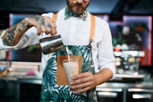Close-up of barista preparing latte coffee in tall drinking glass.