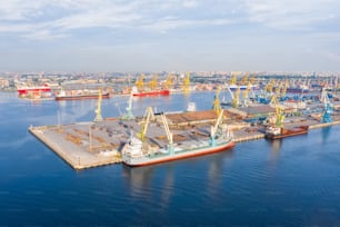 Luftaufnahme riesiges Frachtschiff, das am Pier am Hafen vor Anker liegt und Waren, Metall, Beton und andere feste Rohstoffe lädt