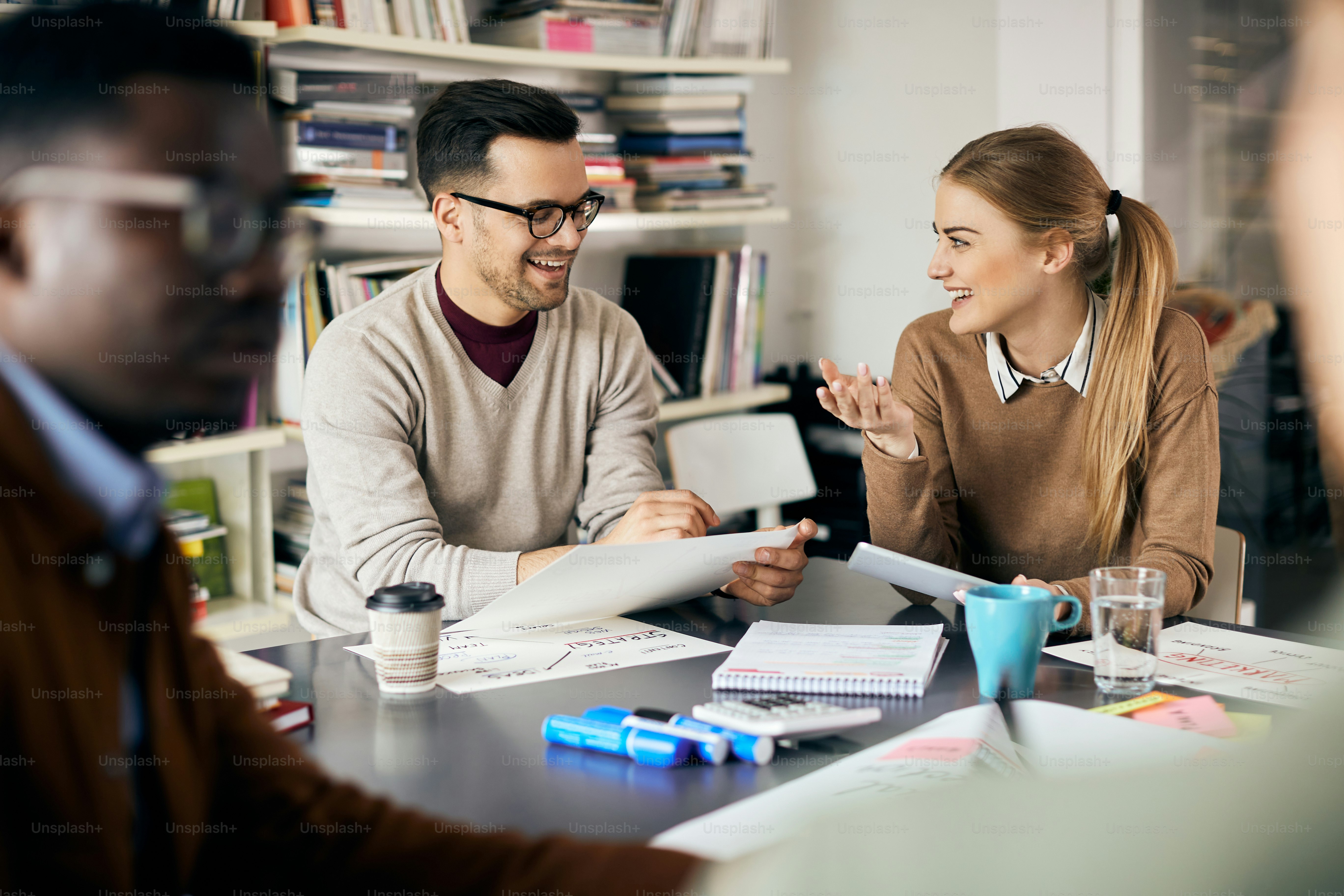 Glücklicher Unternehmer, der Geschäftspläne analysiert und mit einer Kollegin spricht, die während des Meetings das Touchpad verwendet.