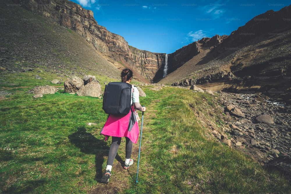 Mulher viajante trekking na paisagem de verão islandesa na cachoeira Hengifoss na Islândia. A cachoeira está situada na parte oriental da Islândia.