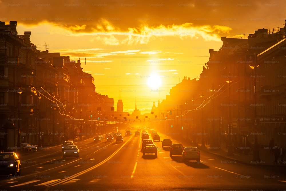 Perspective view of a long central city street with with silhouettes of cars and pedestrians people at sunset bright sun