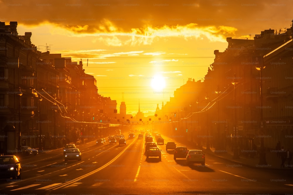 Vue en perspective d’une longue rue centrale de la ville avec des silhouettes de voitures et de piétons au coucher du soleil, soleil éclatant
