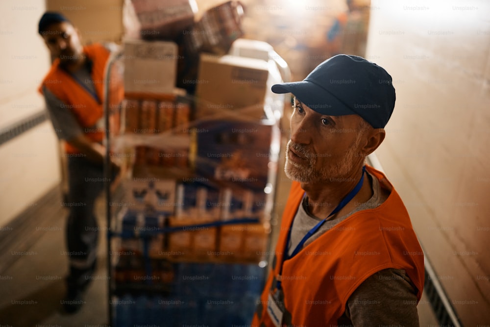 Travailleurs d’entrepôt de distribution déplaçant des rayonnages avec des marchandises tout en travaillant dans le compartiment d’entreposage. L’accent est mis sur les travailleurs d’âge mûr.