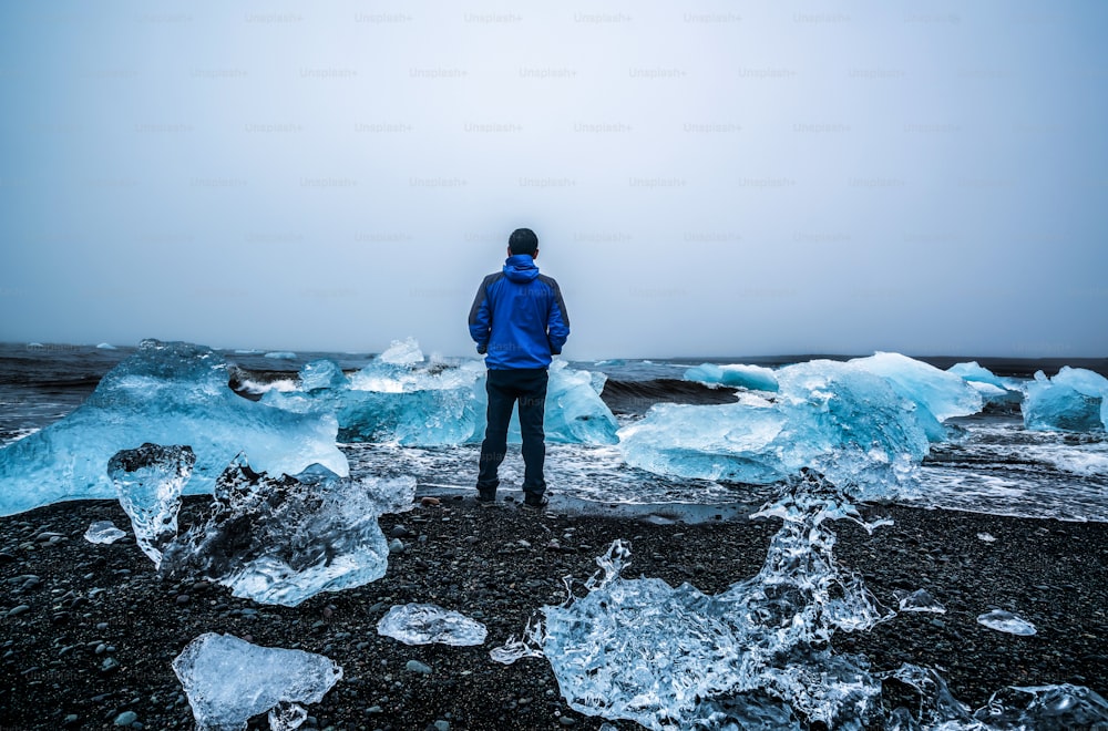 Jeune homme voyageur voyage à Diamond Beach en Islande. La glace gelée sur la plage de sable noir connue s’écoule de la belle lagune glaciaire de Jokulsarlon dans le parc national de Vatnajokull, au sud-est de l’Islande, en Europe.