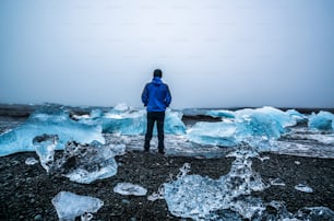 Young man traveler travel to Diamond Beach in Iceland. Frozen ice on black sand beach known flows from Jokulsarlon beautiful Glacial Lagoon in Vatnajokull National Park, southeast Iceland, Europe.