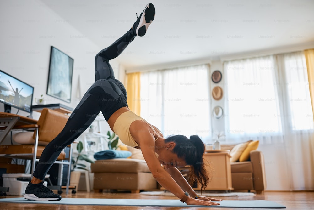 Atleta feminina fazendo exercício de aquecimento de elevação de perna na sala de estar.