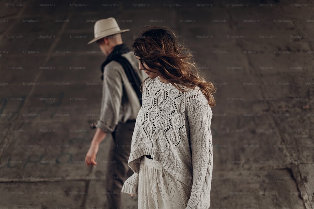 Beautiful sensual indie girl in hipster boho clothes posing in front of handsome cowboy guitar player outdoors