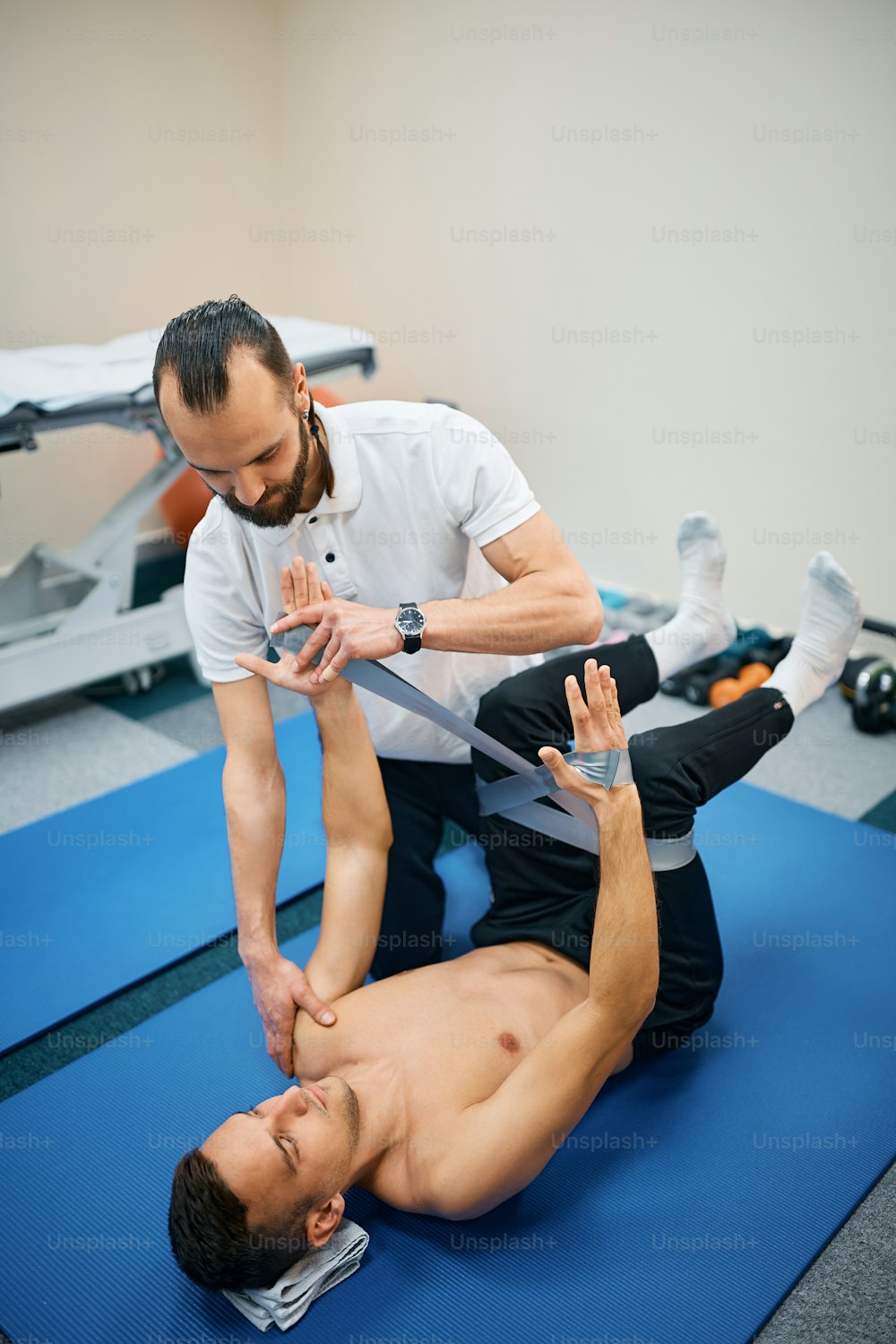 Physical therapist assisting male patient with using power band during the therapy at rehabilitation center.