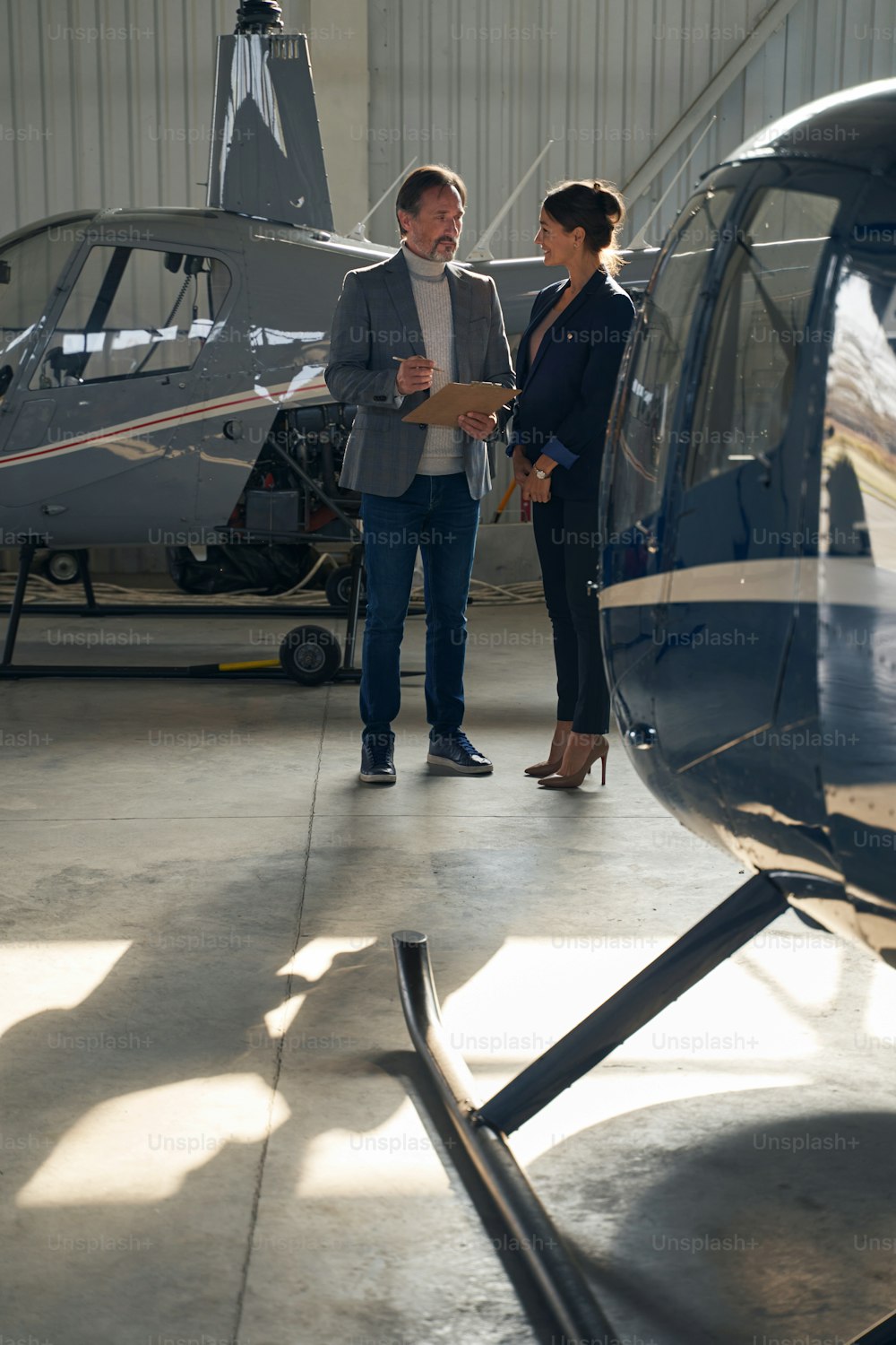 Smiling elegant young Caucasian woman communicating with serious man in aircraft shelter