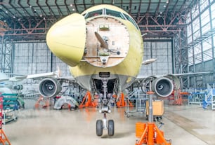 Avión de pasajeros en mantenimiento de reparación de motor y revisión de fuselaje en hangar del aeropuerto. Con un capó abierto en el morro debajo de la cabina de los pilotos