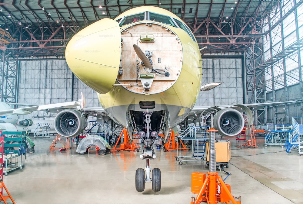 空港の格納庫でエンジンと胴体のメンテナンス修理を行う旅客機。パイロットのコックピット下の機首にオープンフード付き