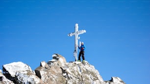 Ein männlicher Backcountry-Skifahrer am Gipfelkreuz eines hochalpinen Gipfels an einem schönen Wintertag