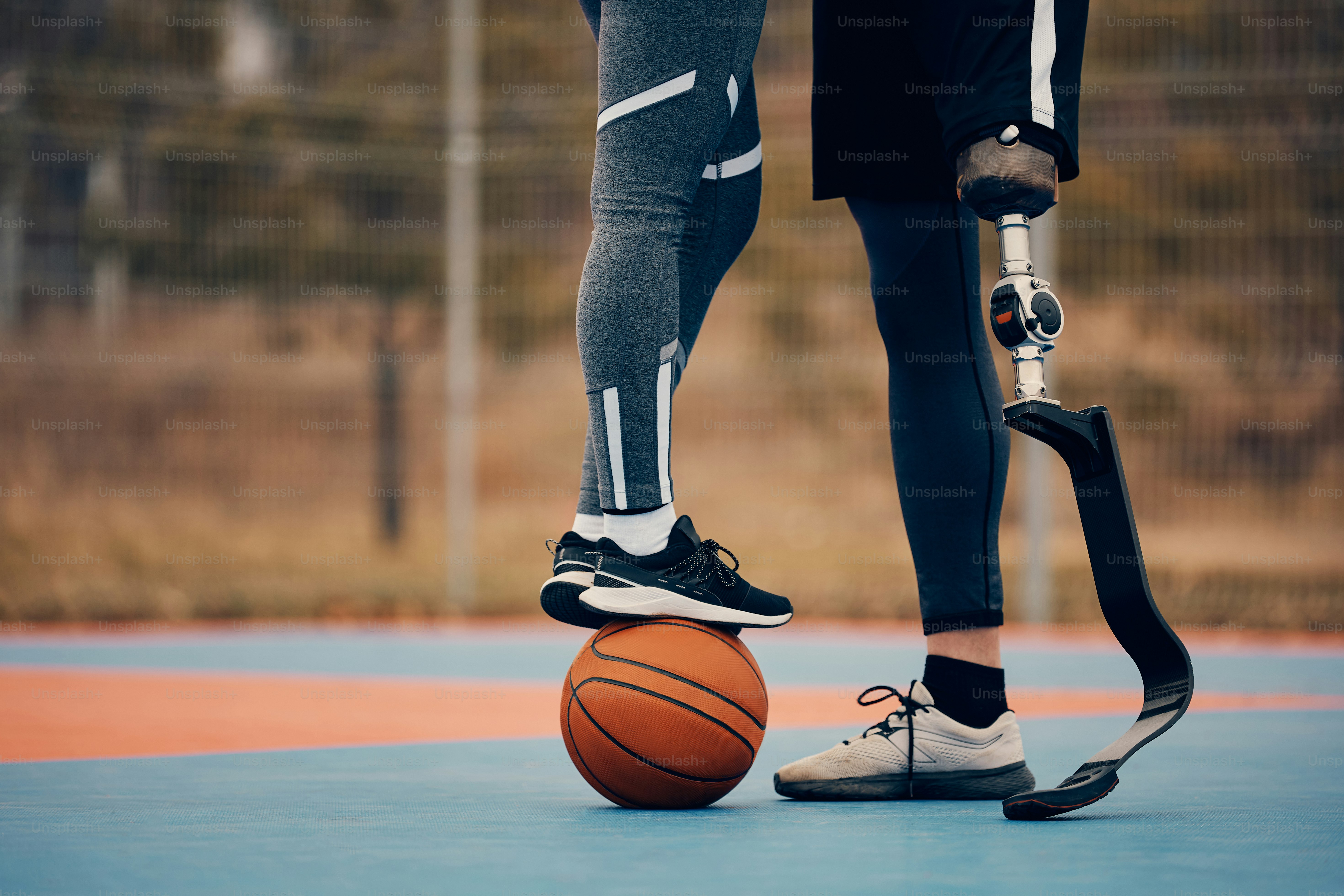 Unkenntlicher Sportler mit künstlichem Bein und seine Freundin, die auf einem Basketball auf einem Sportplatz im Freien steht.