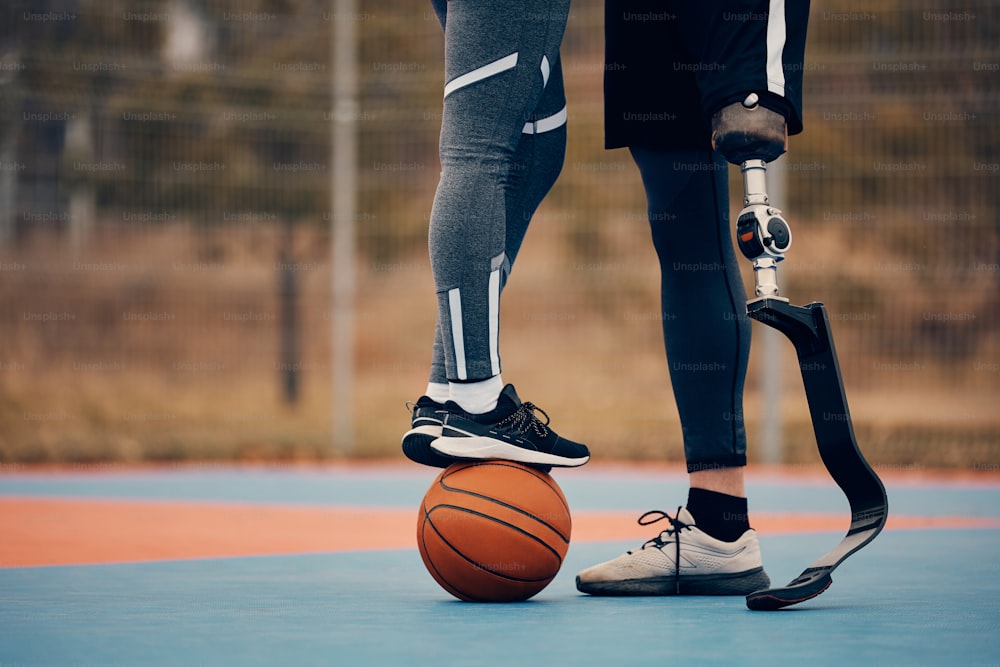 義足を装着した見分けのつかないアスリートと、屋外のスポーツコートでバスケットボールの上に立っているガールフレンド。