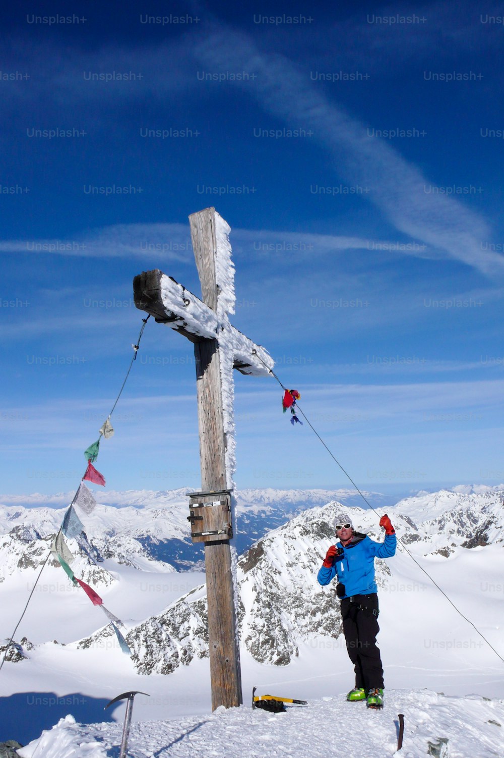 Uno sciatore fuoripista maschio alla croce di vetta di un'alta vetta alpina in una bella giornata invernale