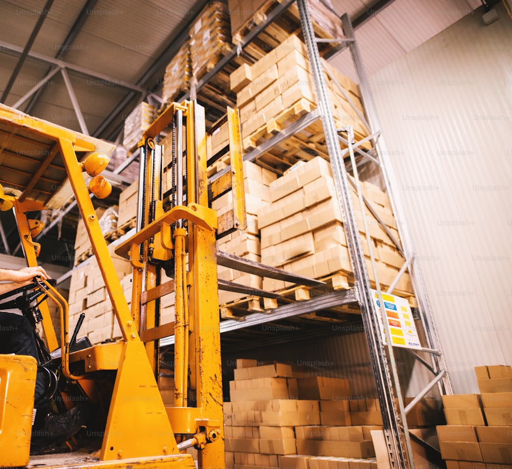 Fork lifter approaching pallet filled with stacks of boxes on a rack in storage area.