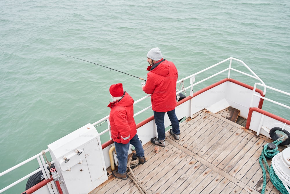 High angle view of the two fishermans holding fishing rod to fighting fish in ocean or at sea. Sport activities or fishery and aquaculture concept. Stock photo