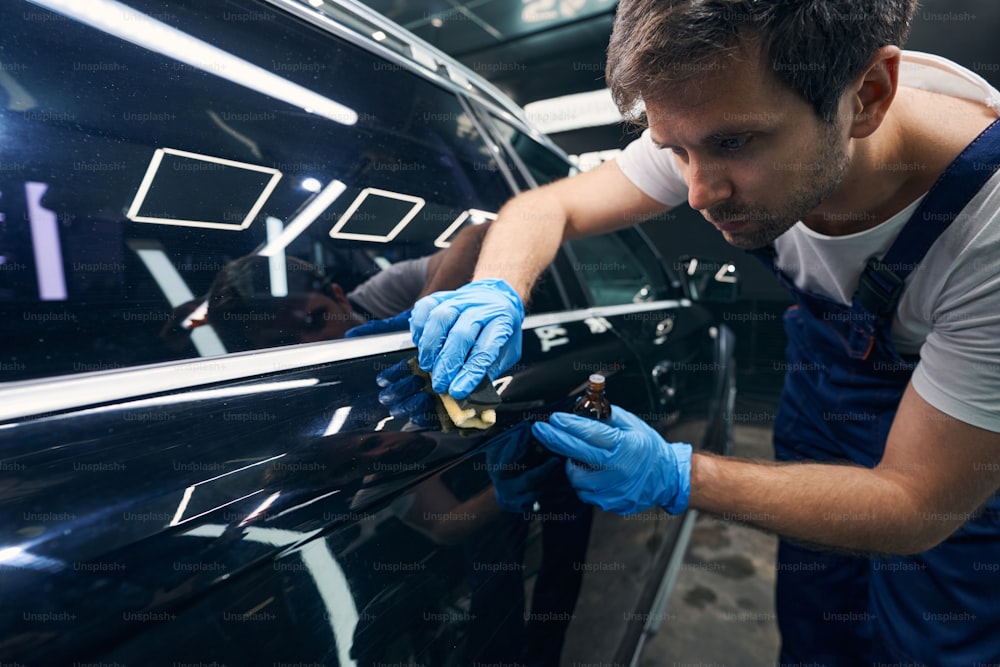 Man using cloth under sponge to cover scratches on car side with ceramic coating from vial