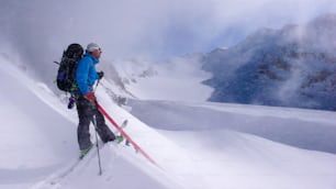 sciatore fuoripista maschio sulla sua strada verso un'alta vetta alpina e giocando e facendo lo sciocco durante una leggera nevicata in una altrimenti bella giornata invernale nelle Alpi svizzere